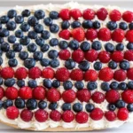 American flag fruit pizza topped with blueberries and strawberries on creamy frosting