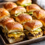 Big Mac-style cheeseburger sliders topped with melted cheese, pickles, and lettuce on sesame buns