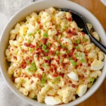 Creamy deviled egg pasta salad topped with bacon bits, chives, and sliced boiled eggs