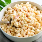 Creamy crowd-size macaroni salad served in a large bowl with fresh vegetables
