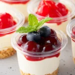 Easy Mini Cheesecake Cups topped with cherry sauce, blueberries, and mint leaves