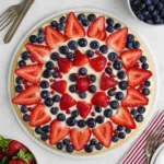 Fourth of July fruit pizza topped with strawberries and blueberries on creamy frosting